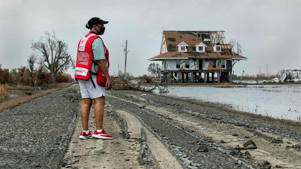 A Red Cross volunteer standing by a home that has been destroyed