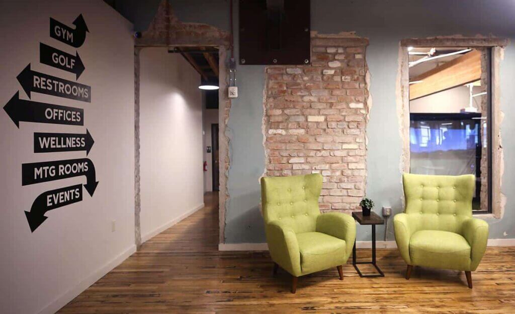 Building lobby with exposed bricks, green arm chairs, and directional signs painted on the wall